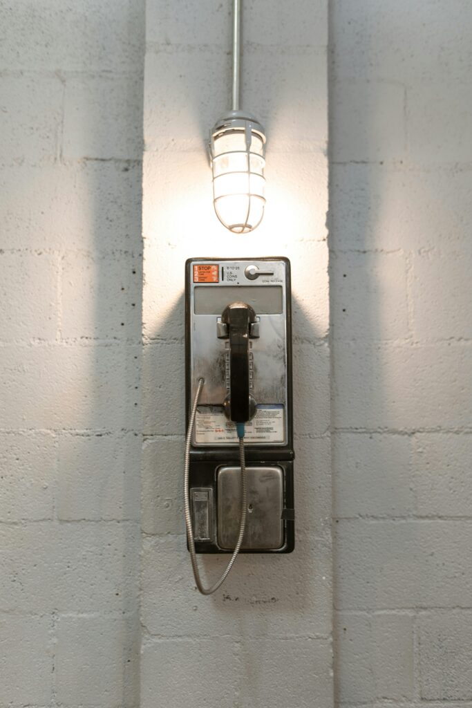 A classic payphone mounted on a white brick wall under a stylish industrial light.